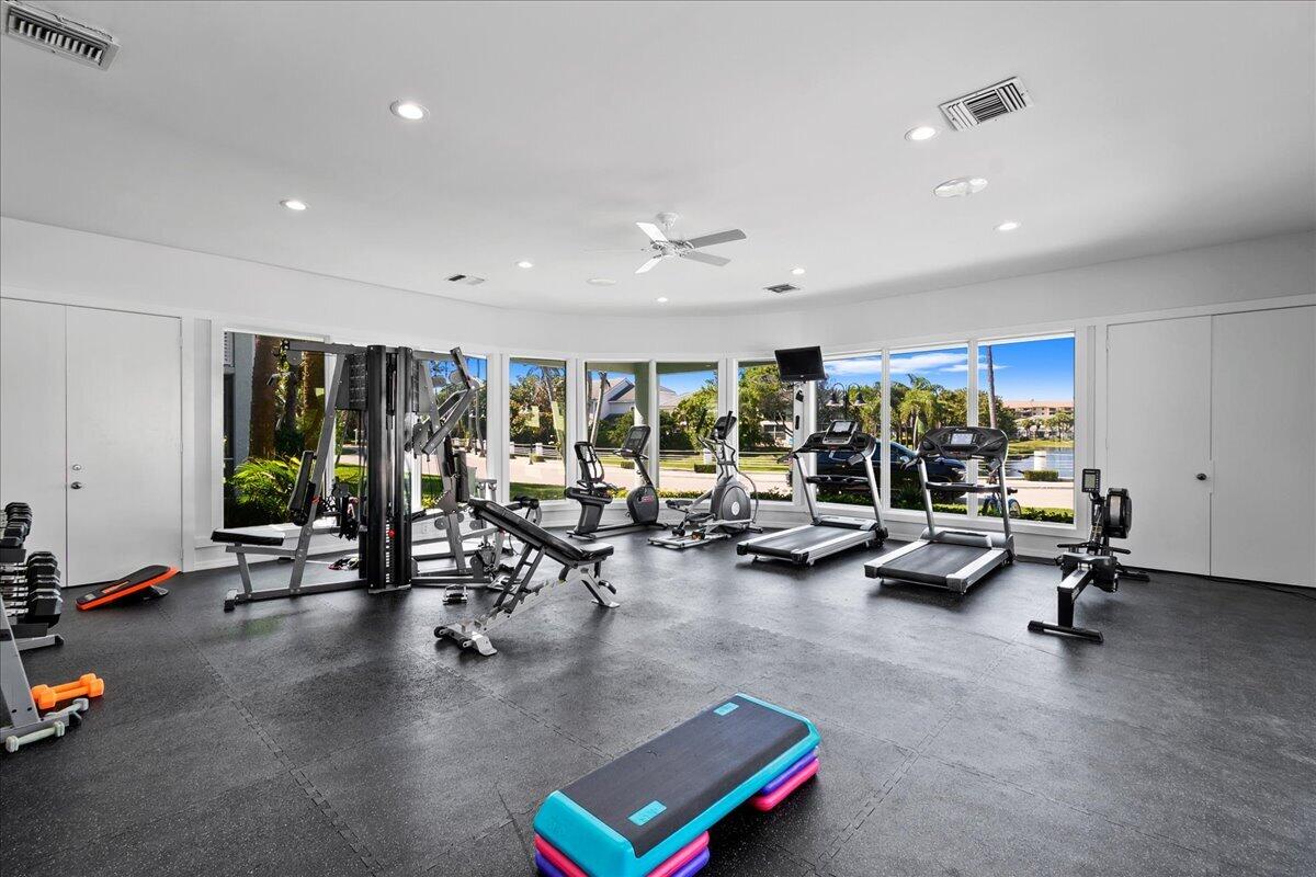 Fitness room with cardio and weight equipment beside large windows overlooking water and palm trees.