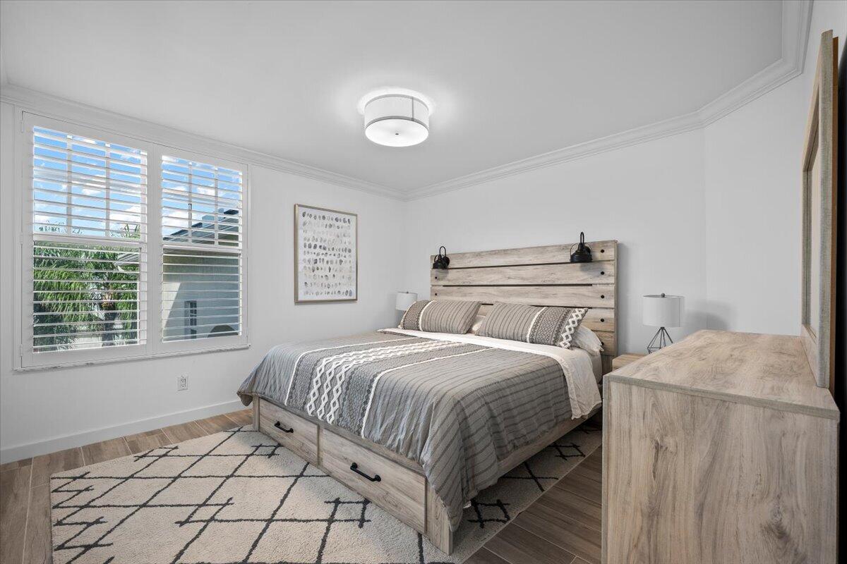 Bedroom with a gray-and-white bed, rustic wood furniture, and plantation-shuttered windows.