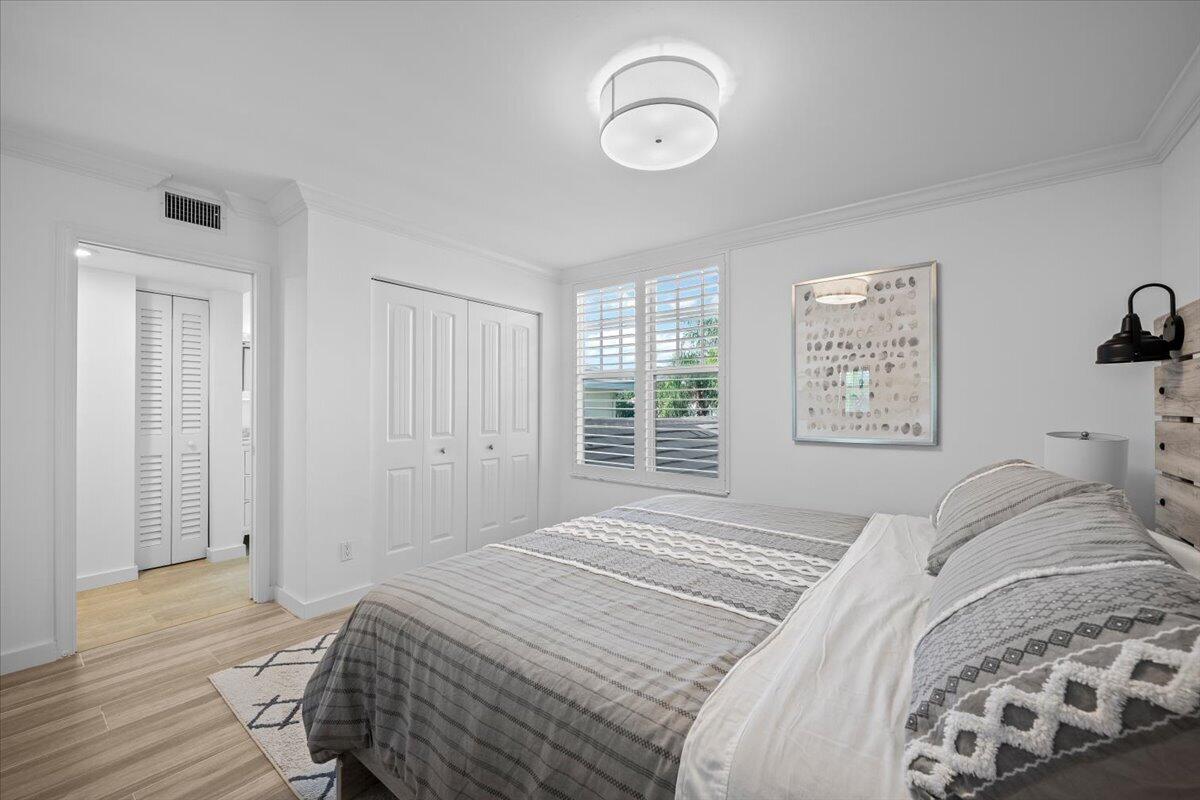 Furnished bedroom with gray patterned bedding, plantation shutters, and light wood flooring.