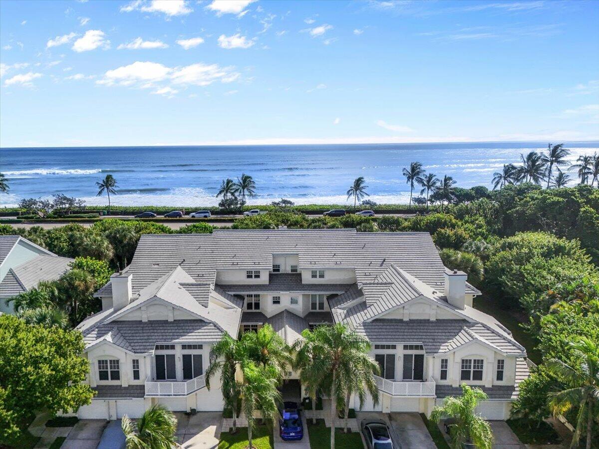 Aerial view of a white coastal residence with the Atlantic Ocean and palm-lined beachfront beyond.