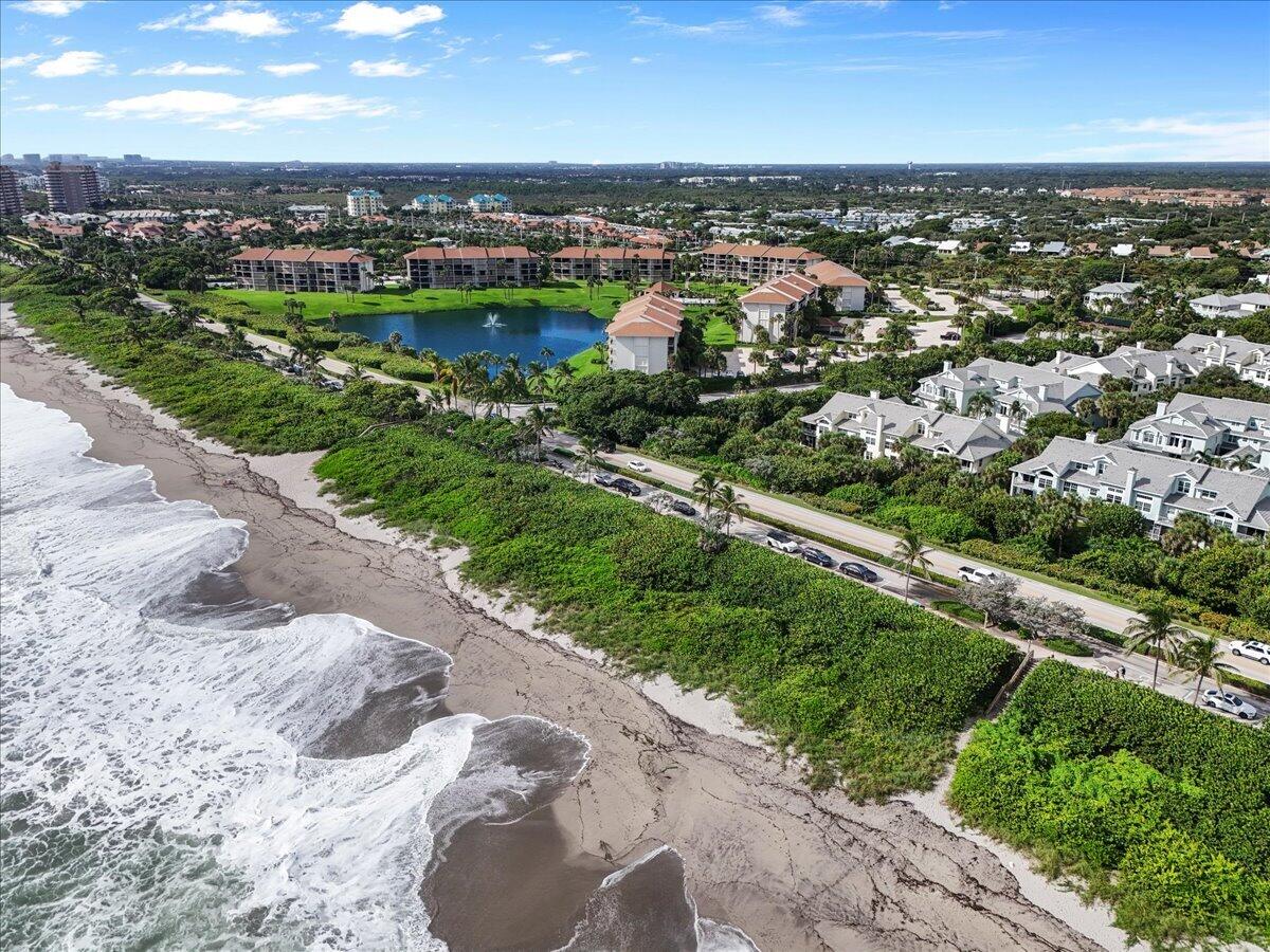 Aerial view of a beachfront community, with ocean waves, sandy shore, homes, and a landscaped pond.