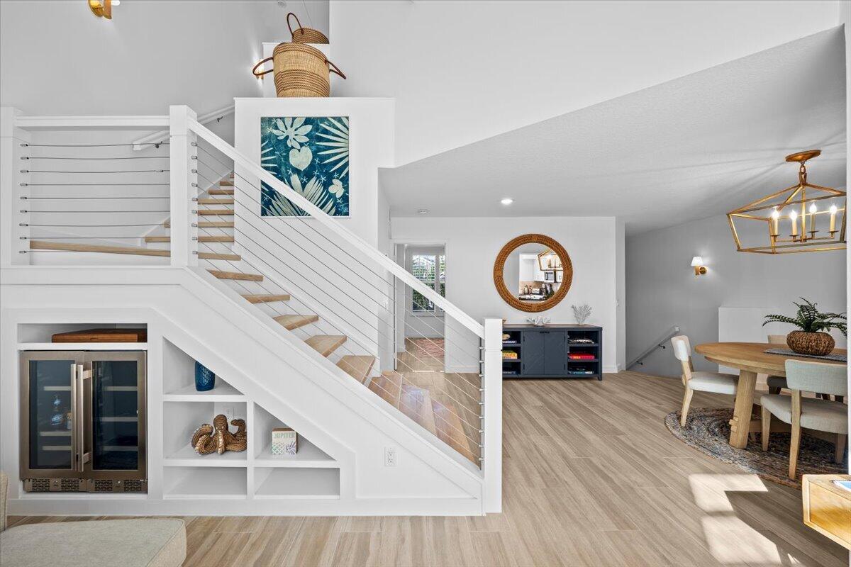 Open-plan dining area beside a white cable-railing staircase and built-in wine refrigerator.