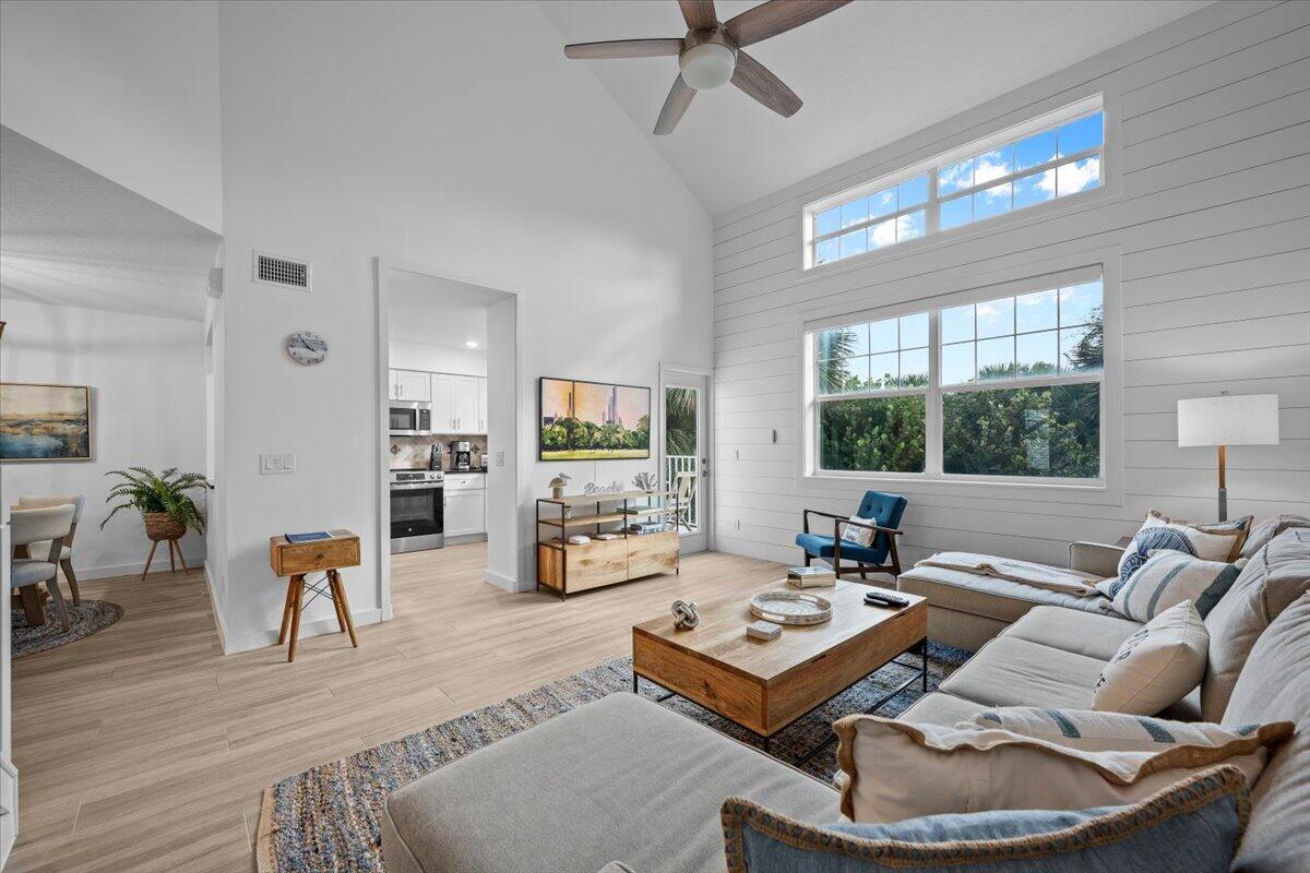 Living room with vaulted ceiling, large windows, and a sectional sofa beside the open kitchen.