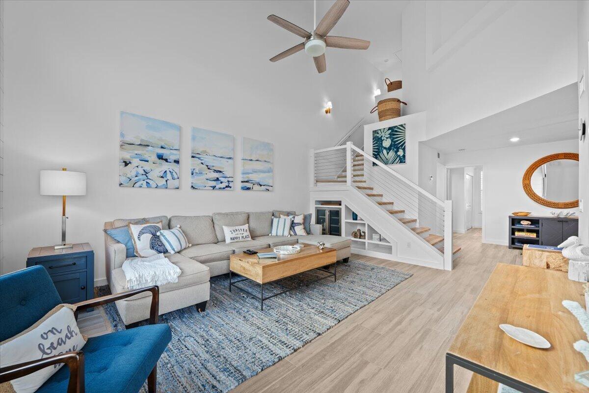 Furnished living room with vaulted ceiling, coastal artwork, gray sectional, and open staircase.