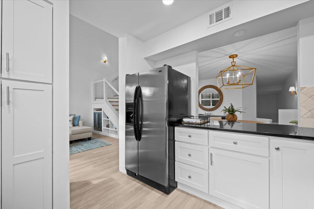Kitchen with white cabinetry, dark countertops, stainless refrigerator, and a gold geometric pendant.