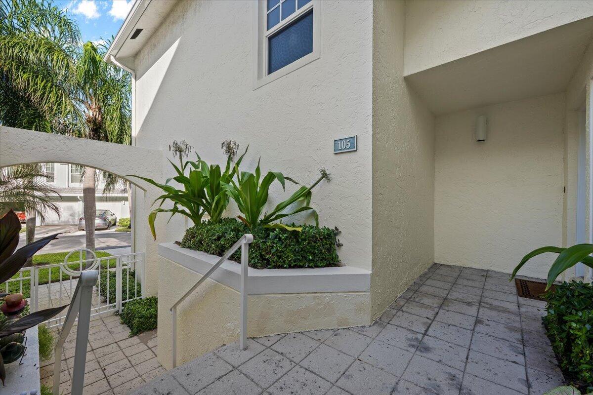 Home entrance marked 105, with a covered doorway, tiled courtyard, tropical plants, and stairs.