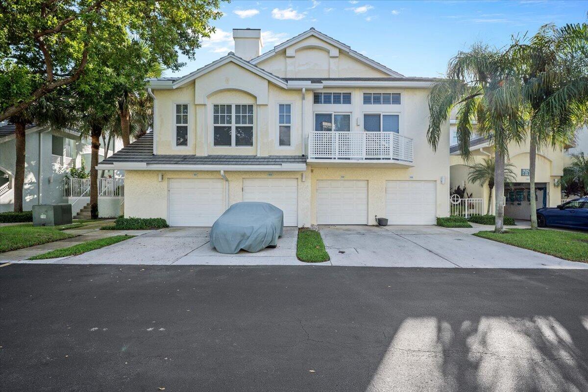Two-story cream home with multiple garage doors, a white balcony, and a covered car in the driveway.