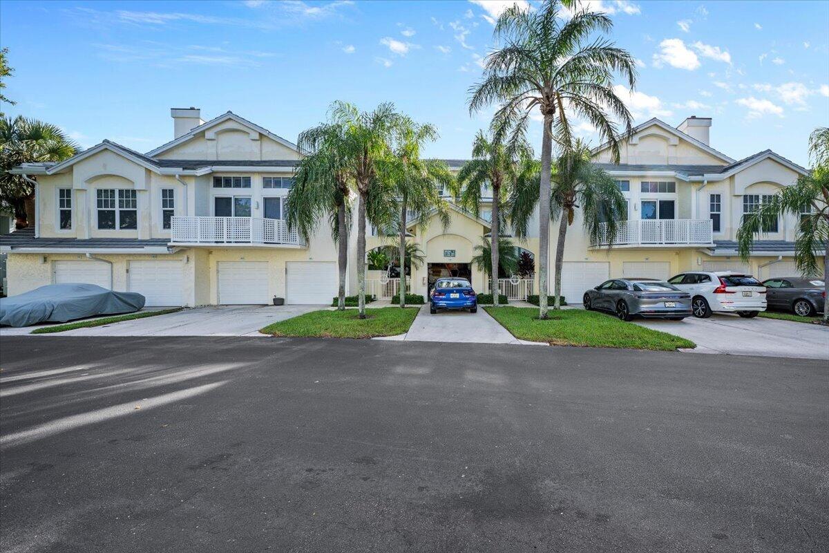 Cream two-story townhomes with white garage doors, balconies, and palm trees along the street.