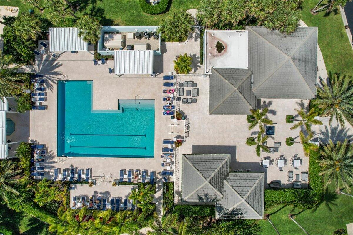 Aerial view of a turquoise pool surrounded by lounge chairs, shade structures, and landscaped patios.