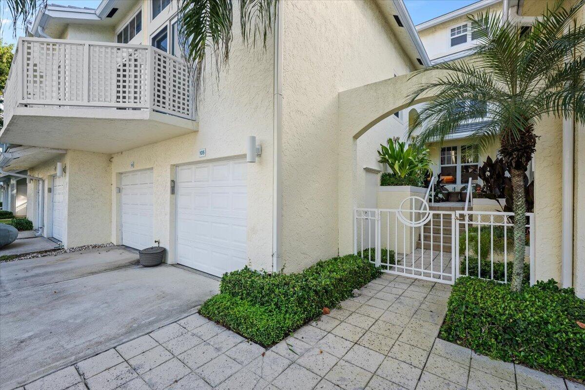 Cream stucco residence with a tiled gated entry, palms, balcony, and garage.