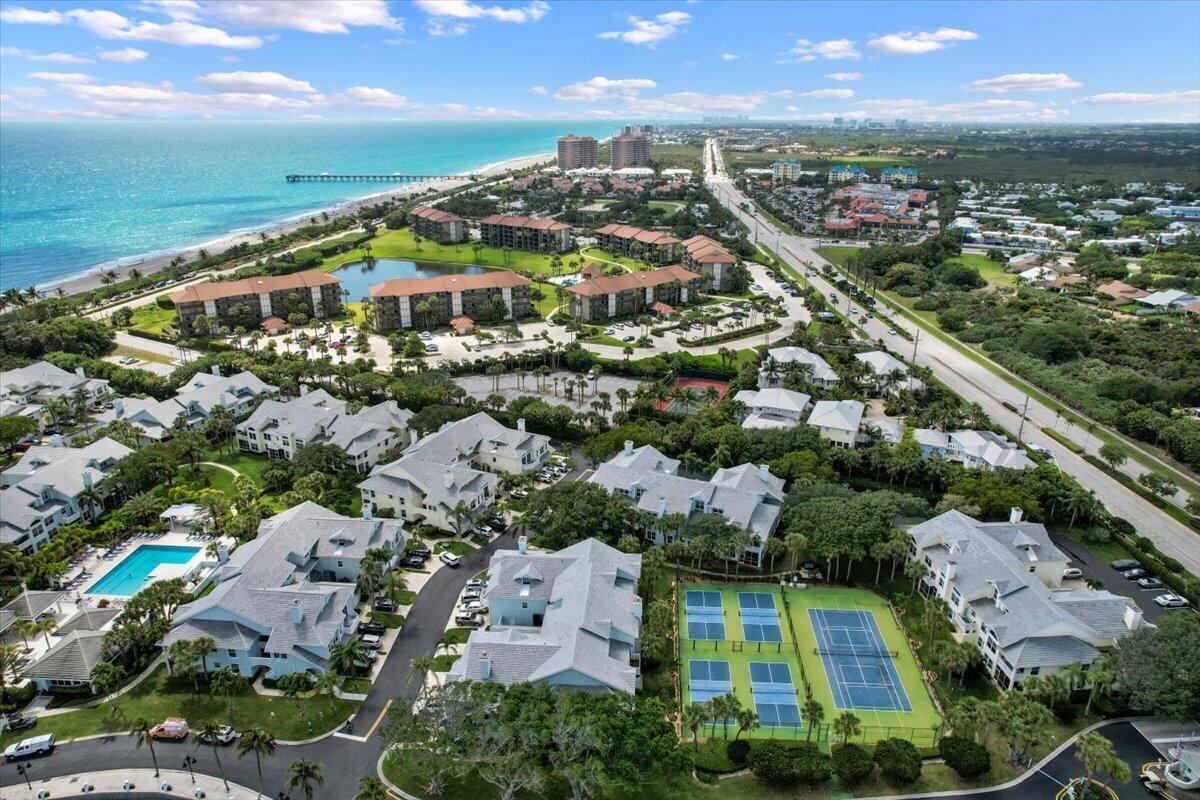 Aerial view of coastal condos, with the ocean and beach, a pier, pools, and tennis courts.