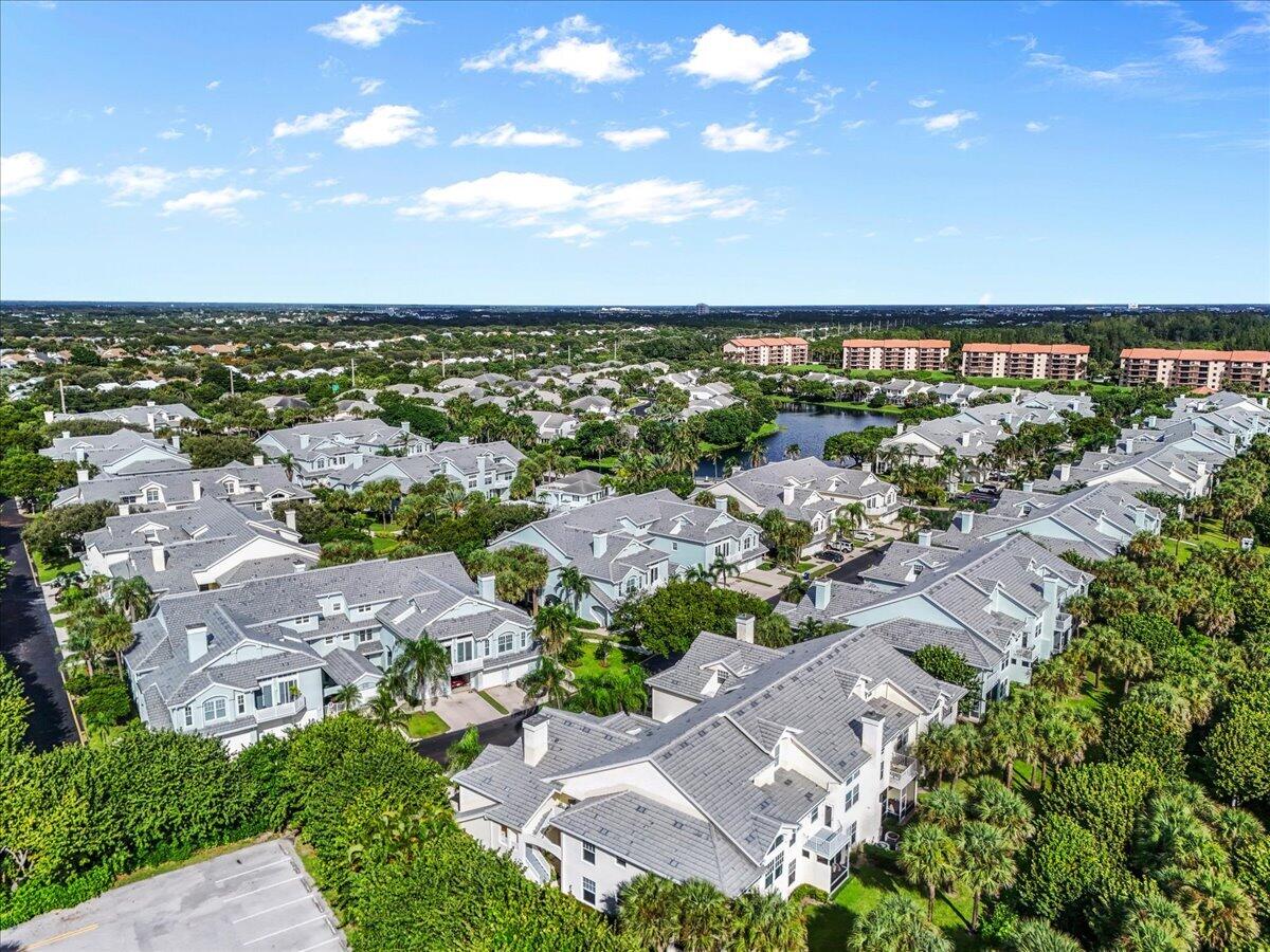 Aerial view of a residential community with gray-roofed homes, palm trees, and a small lake.