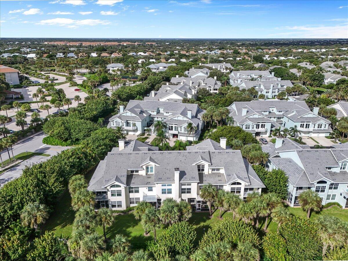 Aerial view of a light-colored home with gray tiled roofs and palms, surrounded by a residential neighborhood.