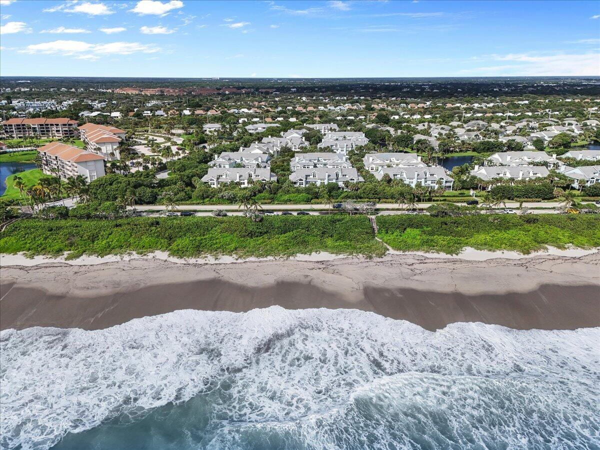 Aerial view of beachfront homes and condos behind a sandy shore, with ocean waves in the foreground.