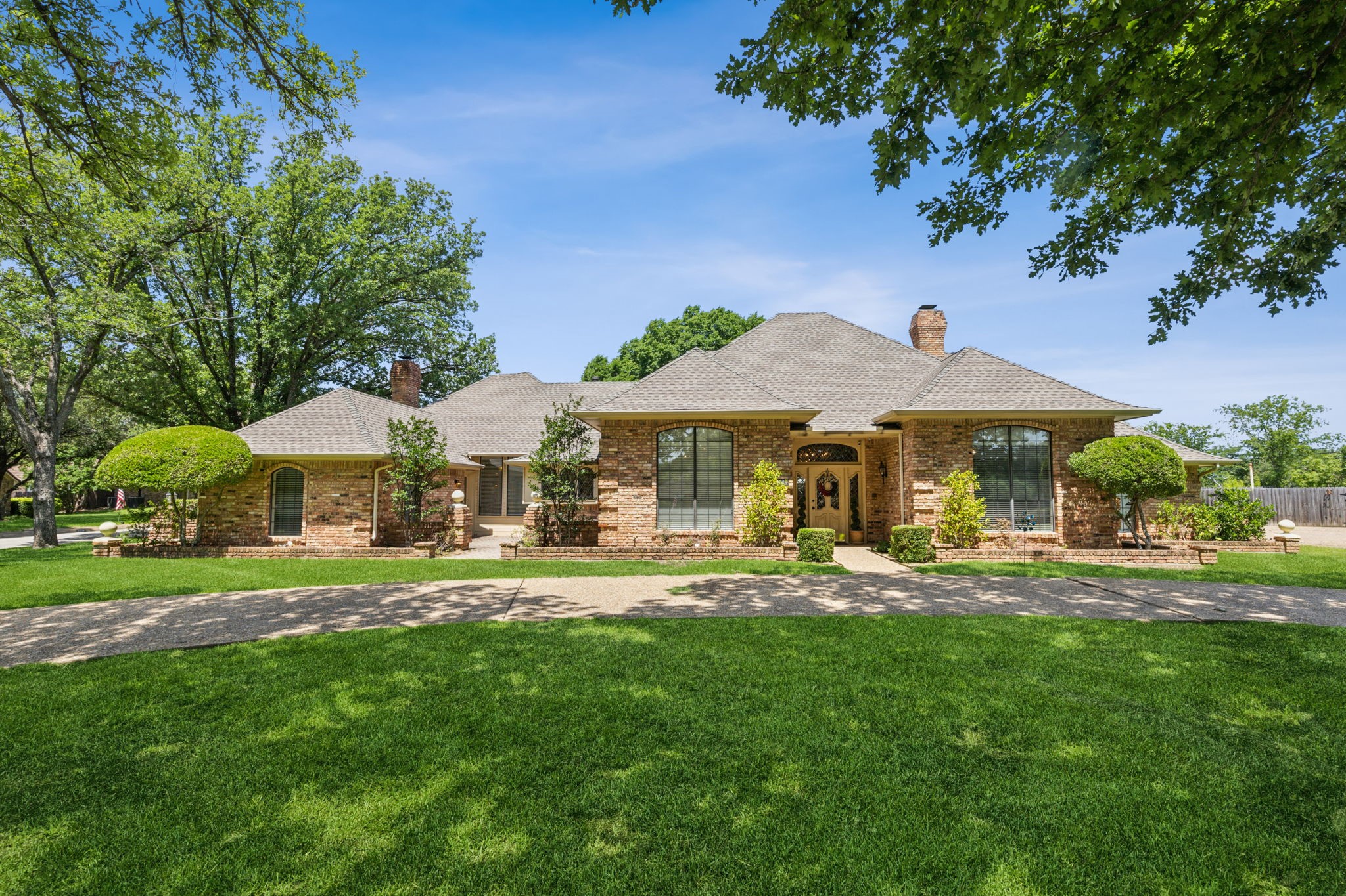Single-story brick home with arched windows, a curved driveway, and a broad green lawn.
