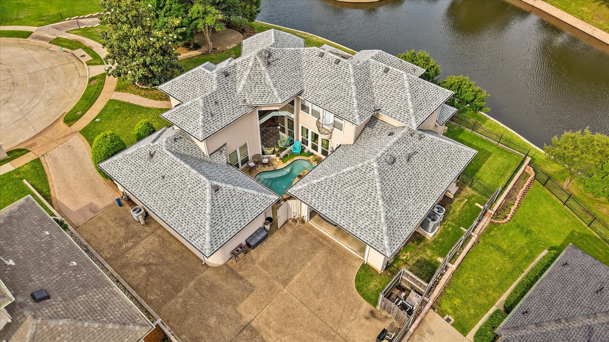 Aerial view of a large lakeside home with a gray roof and courtyard pool.