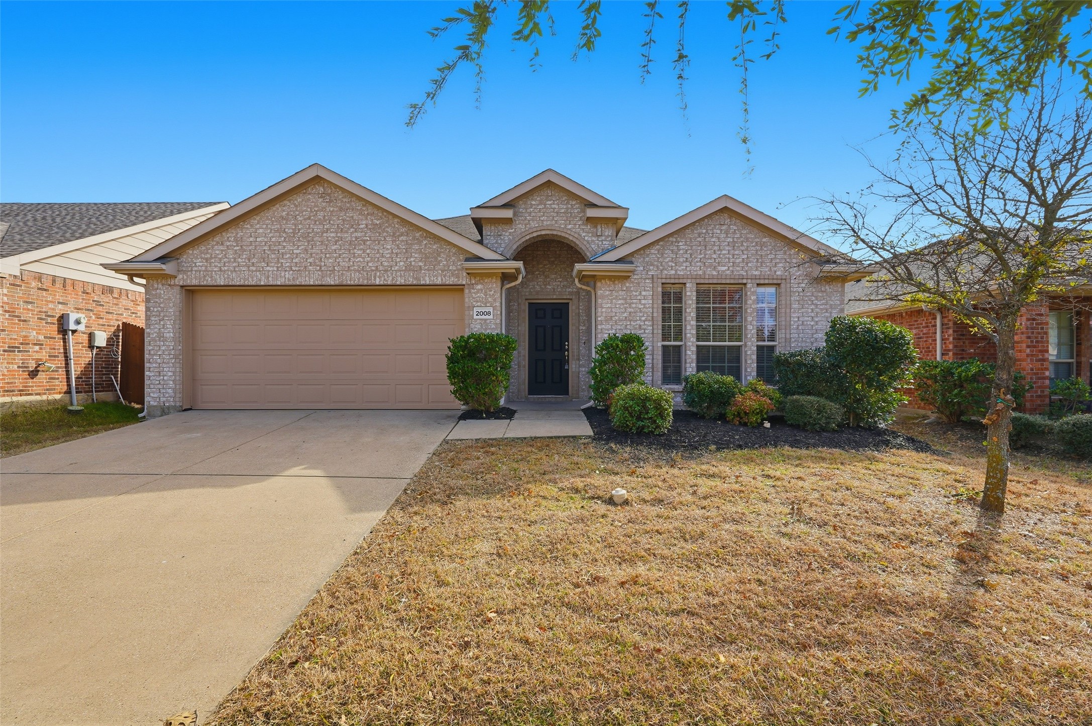 Brick house with a two-car garage, arched entry, and shrubs along the front facade.