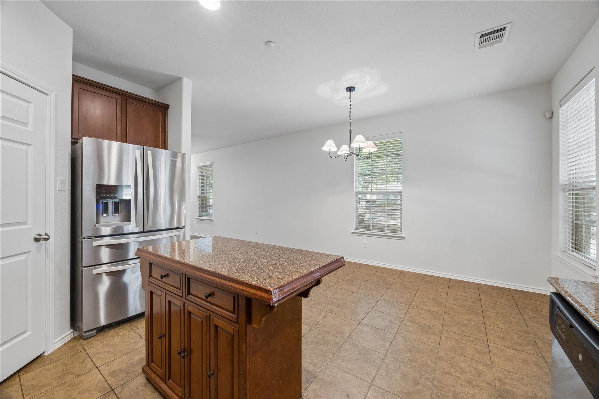 Kitchen and dining area with a granite-topped wood island, stainless steel refrigerator, and tiled floor.