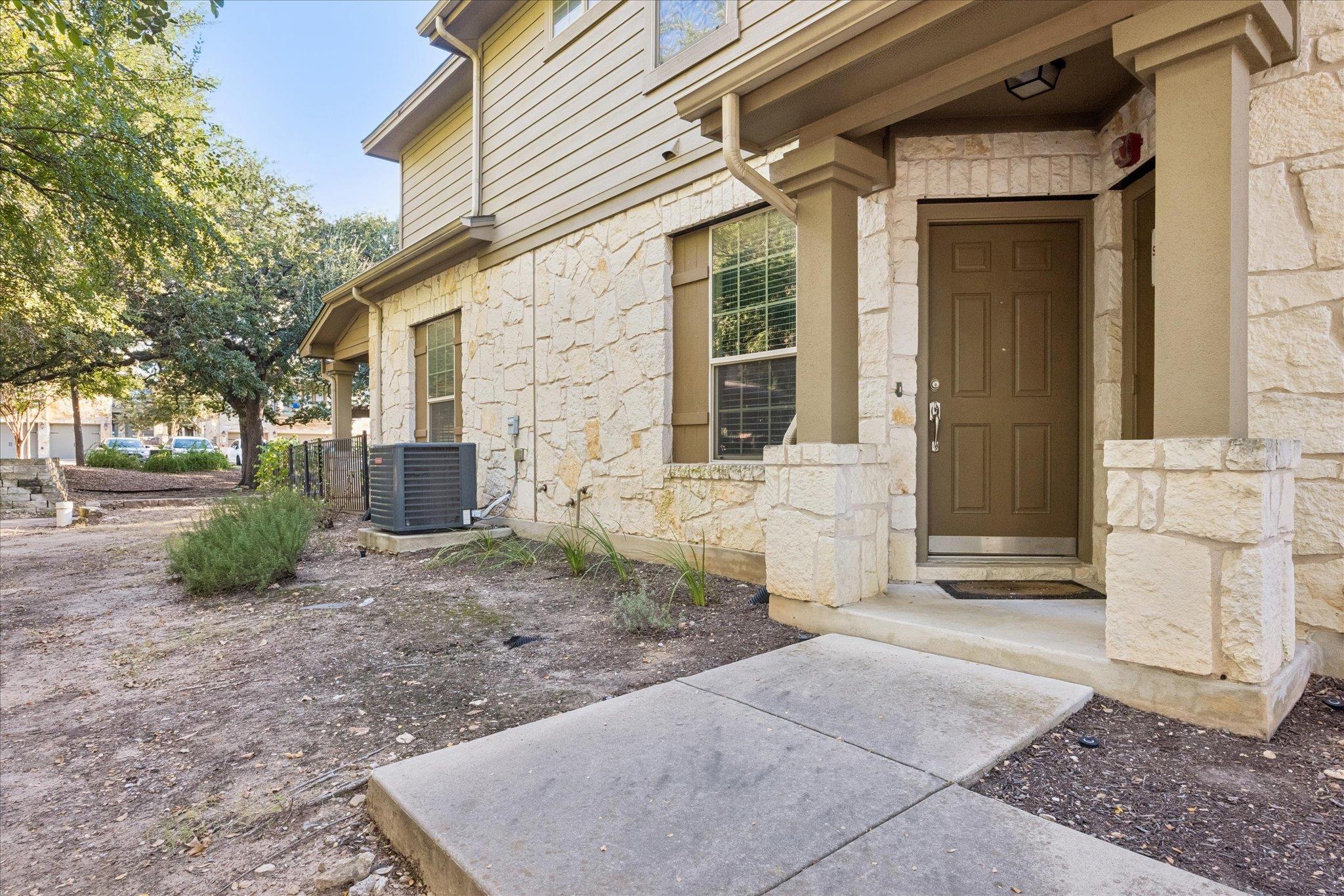 Covered home entrance with a brown door, light stone facade, and concrete walkway.