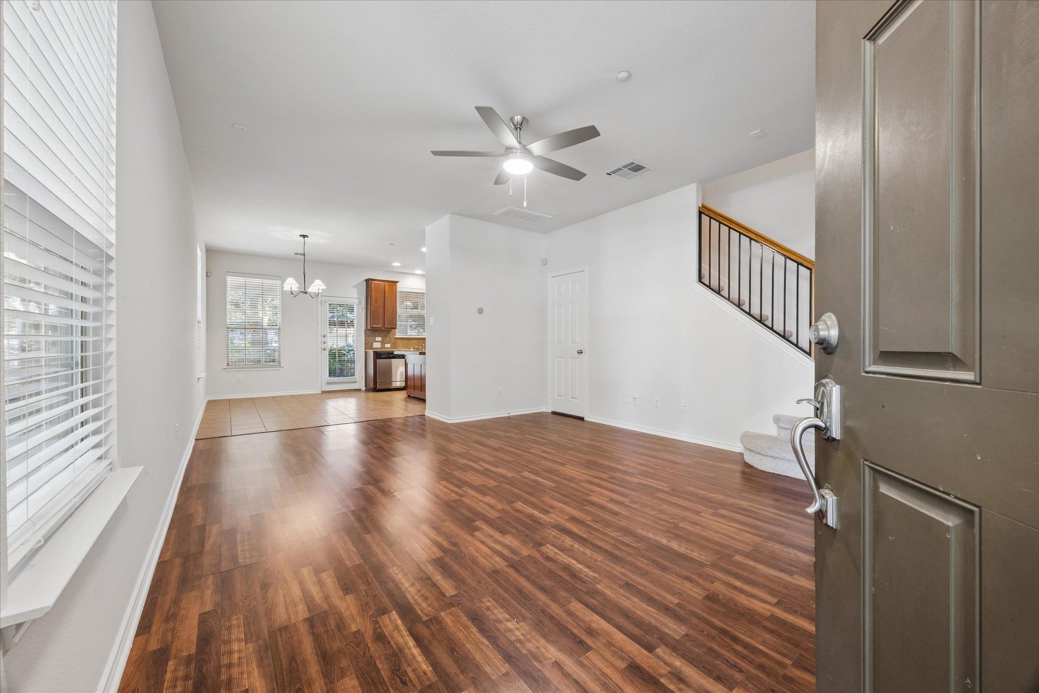 Vacant living room with dark wood-look floors, a ceiling fan, and stairs beside the open front door.