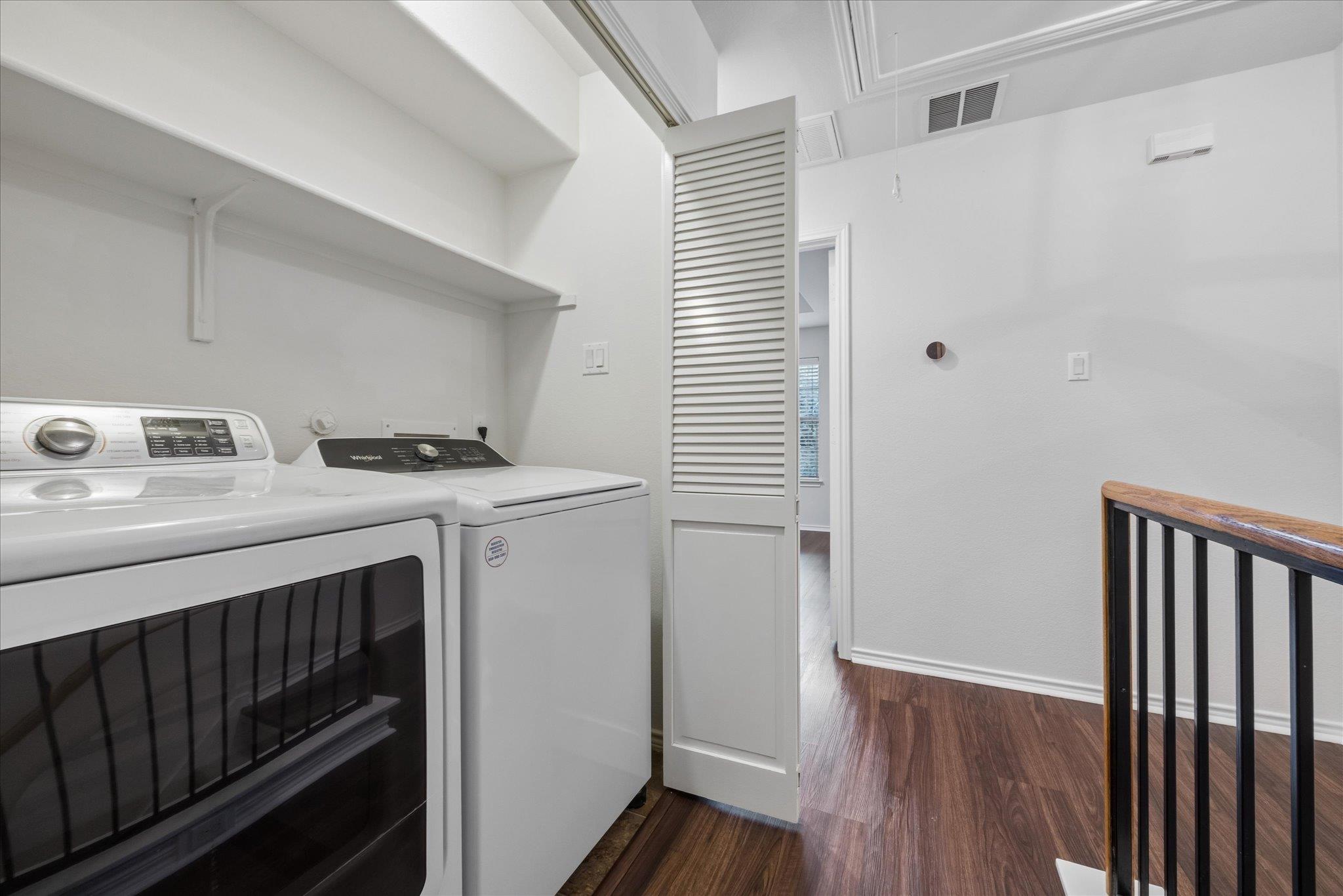 Laundry area with a front-loading dryer, top-loading washer, and open louvered door.