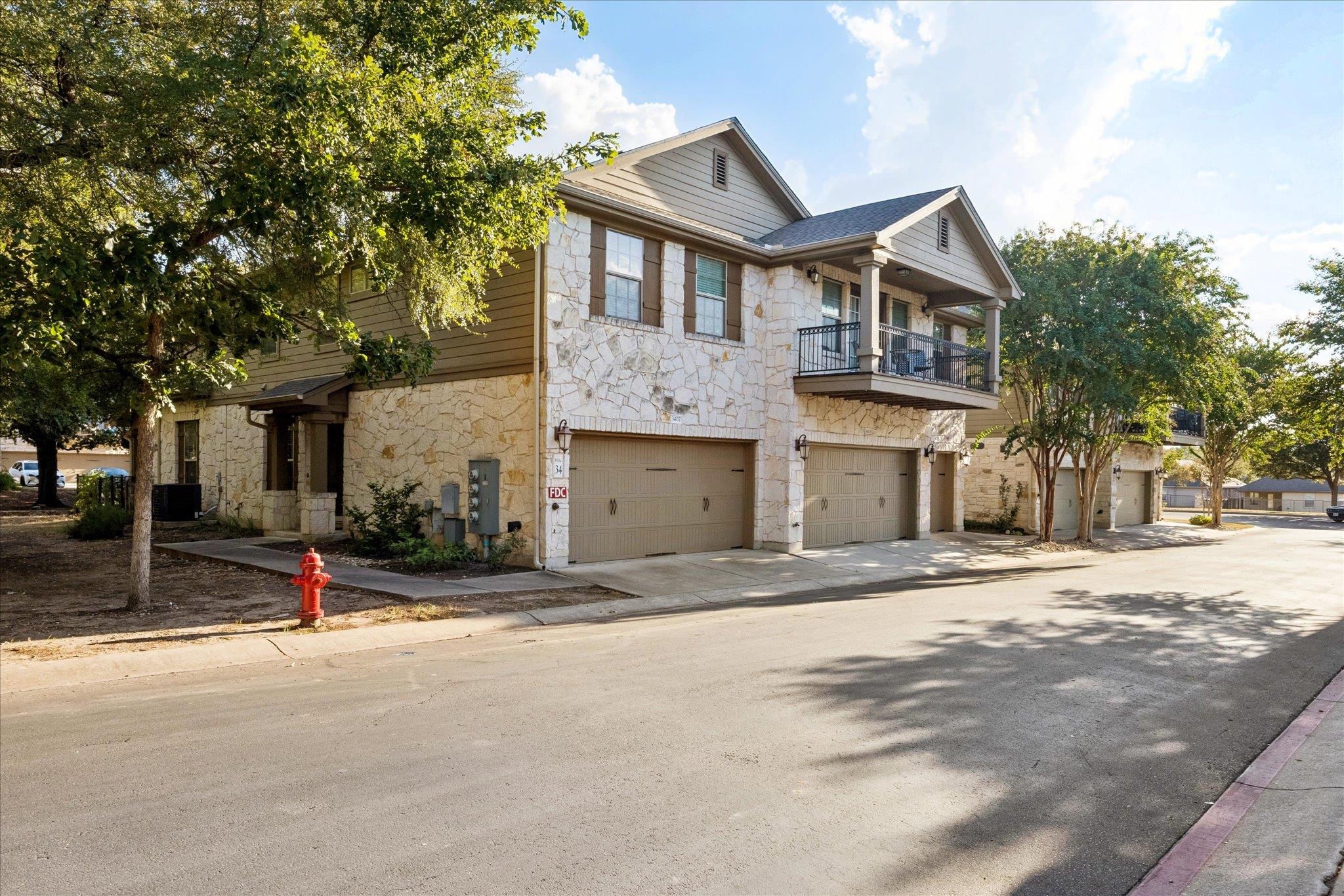 Stone-front condominium building with balconies, garages, and mature trees along the street.