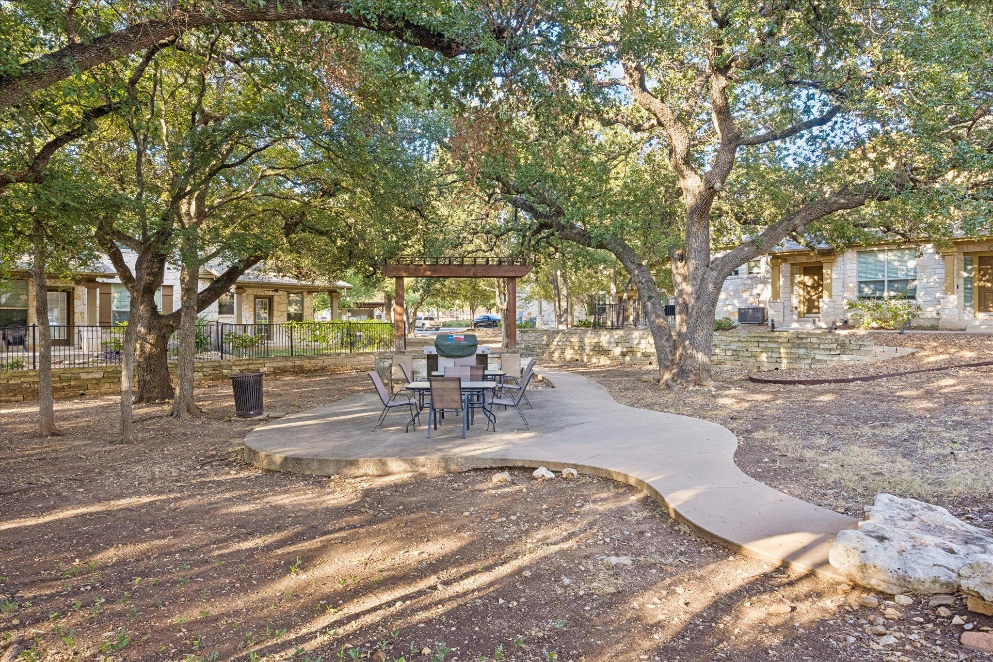 Community courtyard with patio seating beneath mature trees and a wooden pergola.