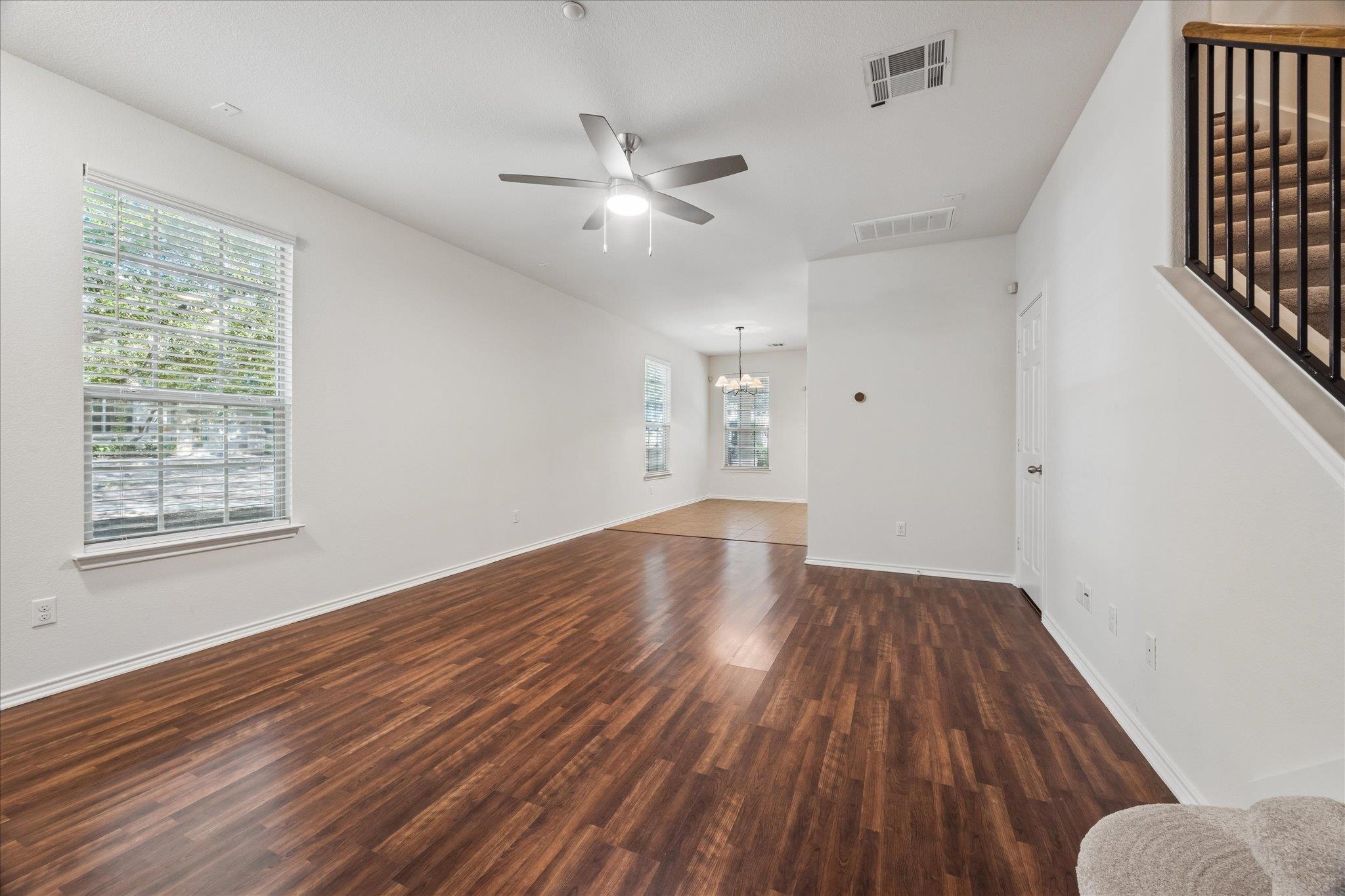 Unfurnished living and dining area with dark wood floors, a ceiling fan, and a staircase with dark railing.