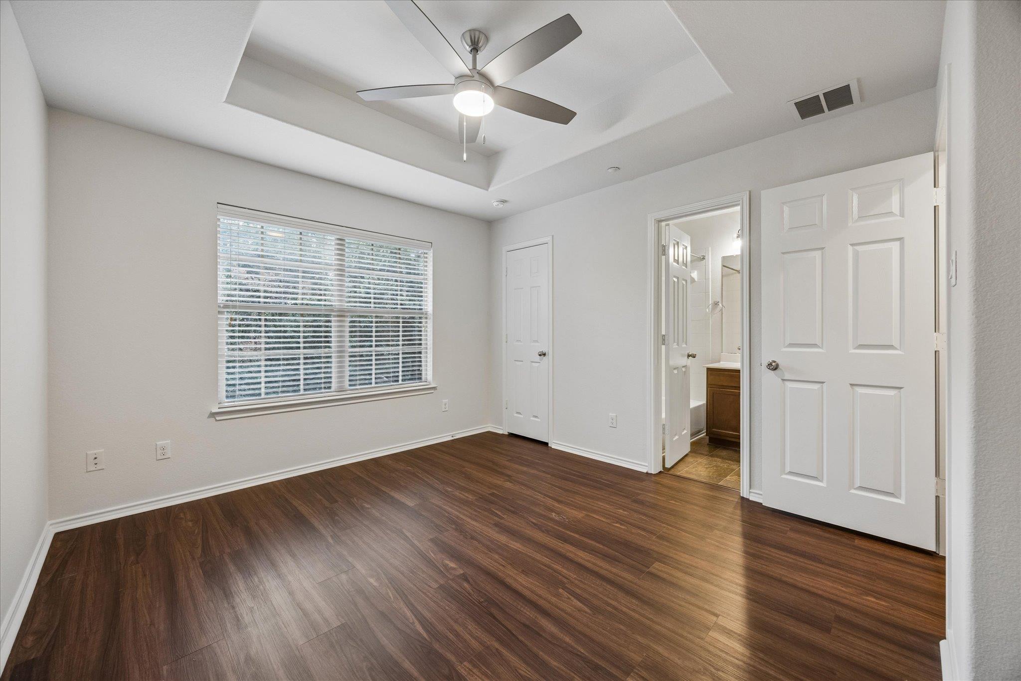 Empty bedroom with dark wood-look floors, a tray ceiling, and an open doorway to the bathroom.