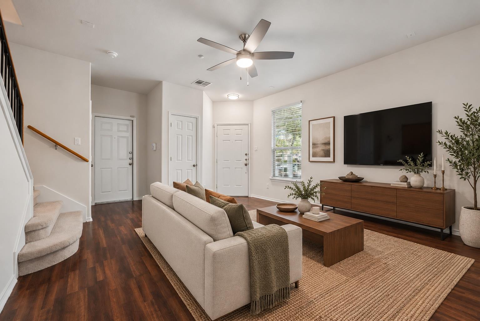 Furnished living room with a beige sofa, dark hardwood floors, and a carpeted staircase.