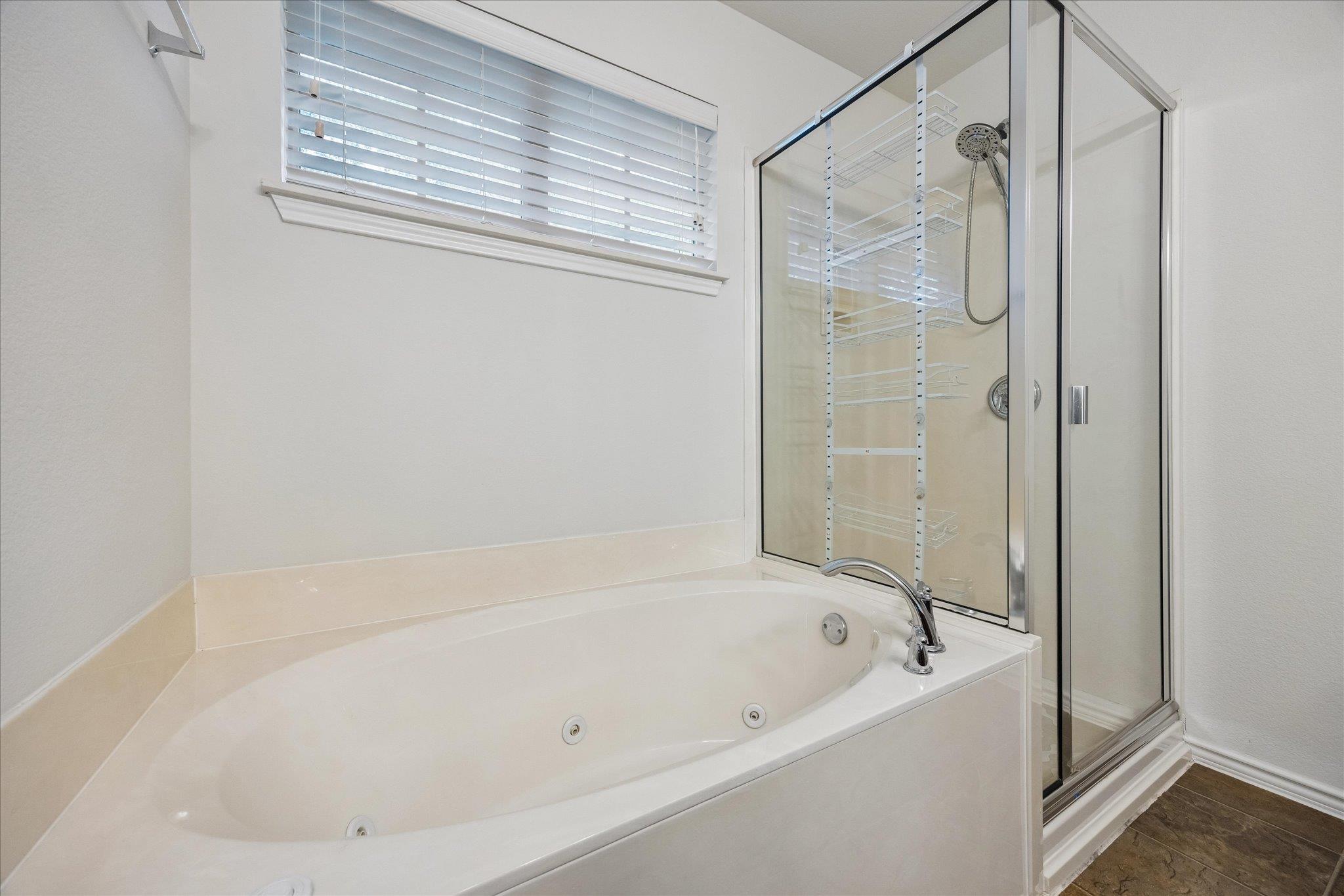 Bathroom with a jetted soaking tub beside a glass-enclosed shower with built-in shelves.