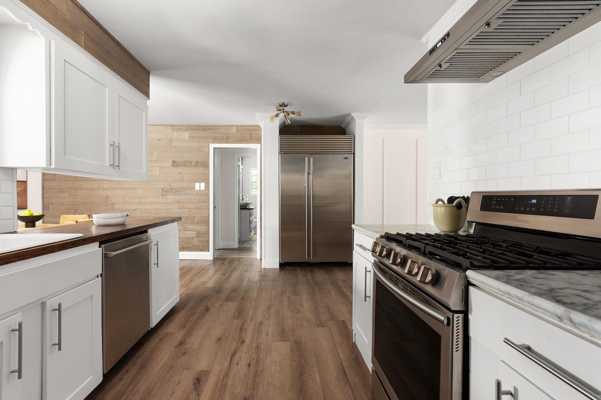 Kitchen with white cabinets, stainless steel appliances, a large gas range, and a wood accent wall.