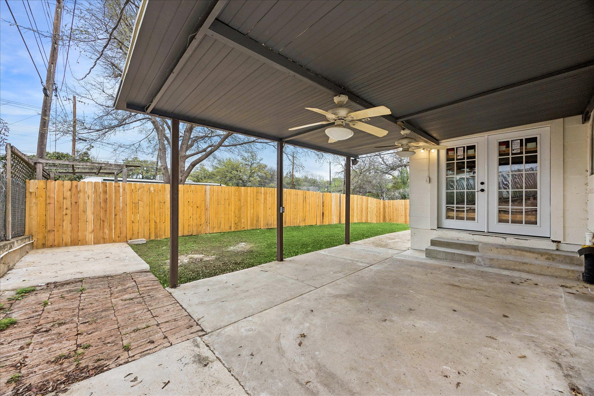 Covered backyard patio with ceiling fans, brick pavers, and a fenced lawn.