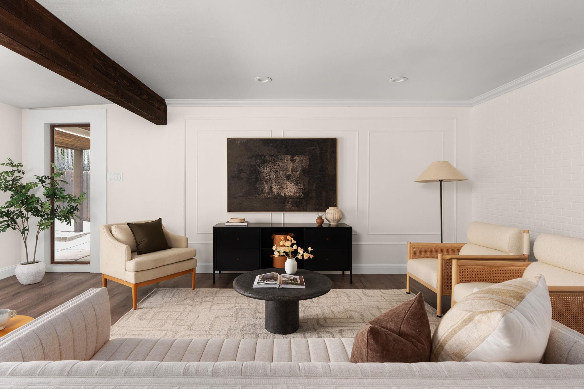 Furnished living room with cream seating, a dark ceiling beam, and a black console beneath abstract art.