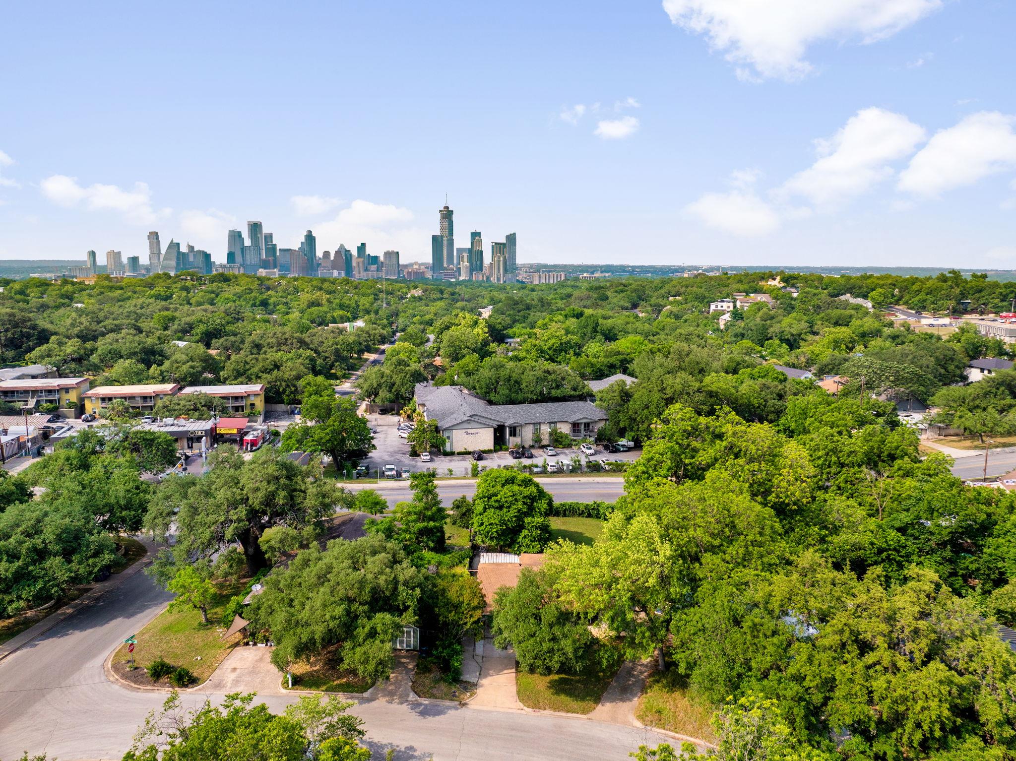Aerial view of a leafy Austin neighborhood with downtown skyline in the distance.