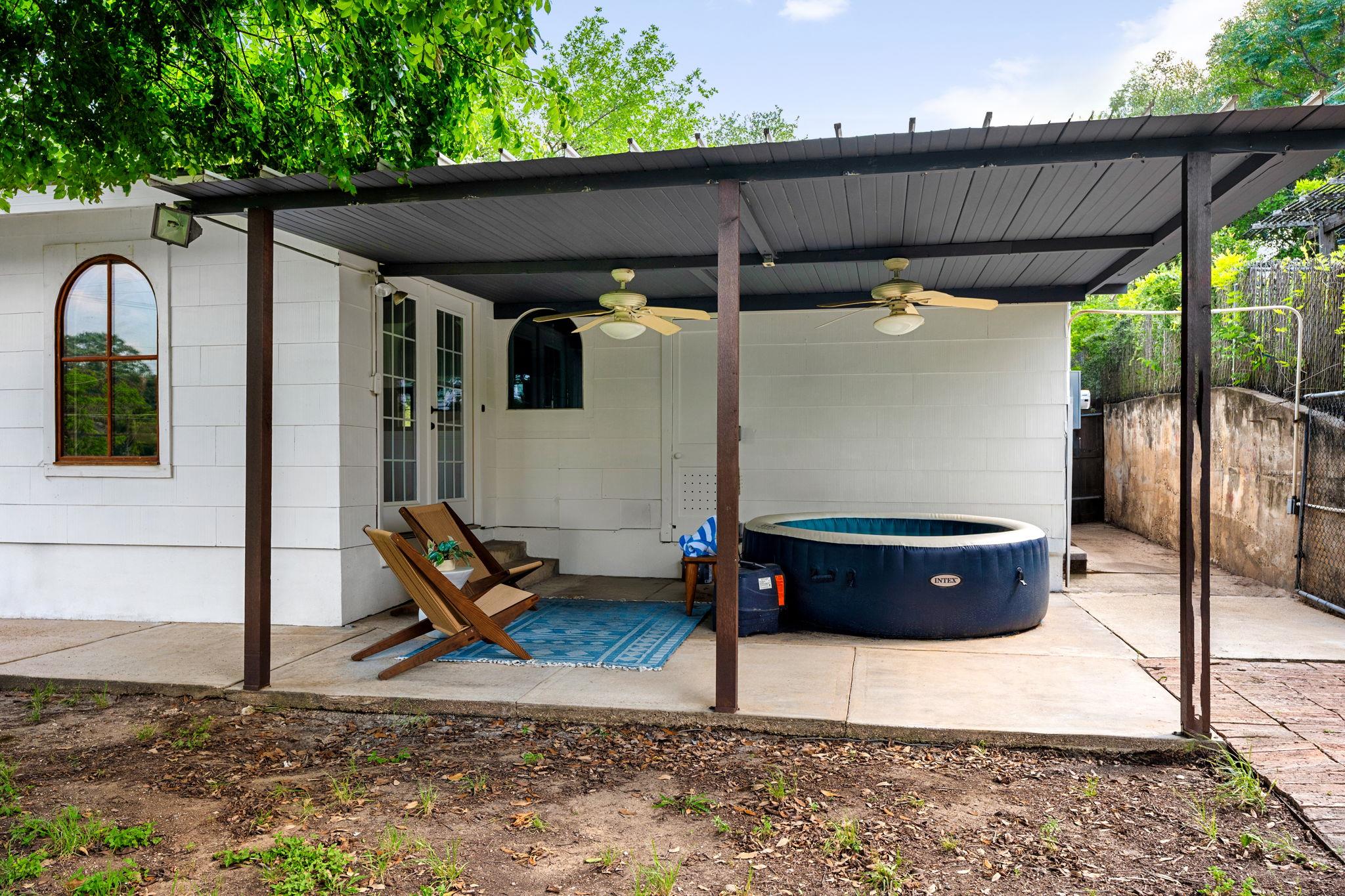 Covered backyard patio with wooden lounge chairs, ceiling fans, and a round inflatable hot tub.