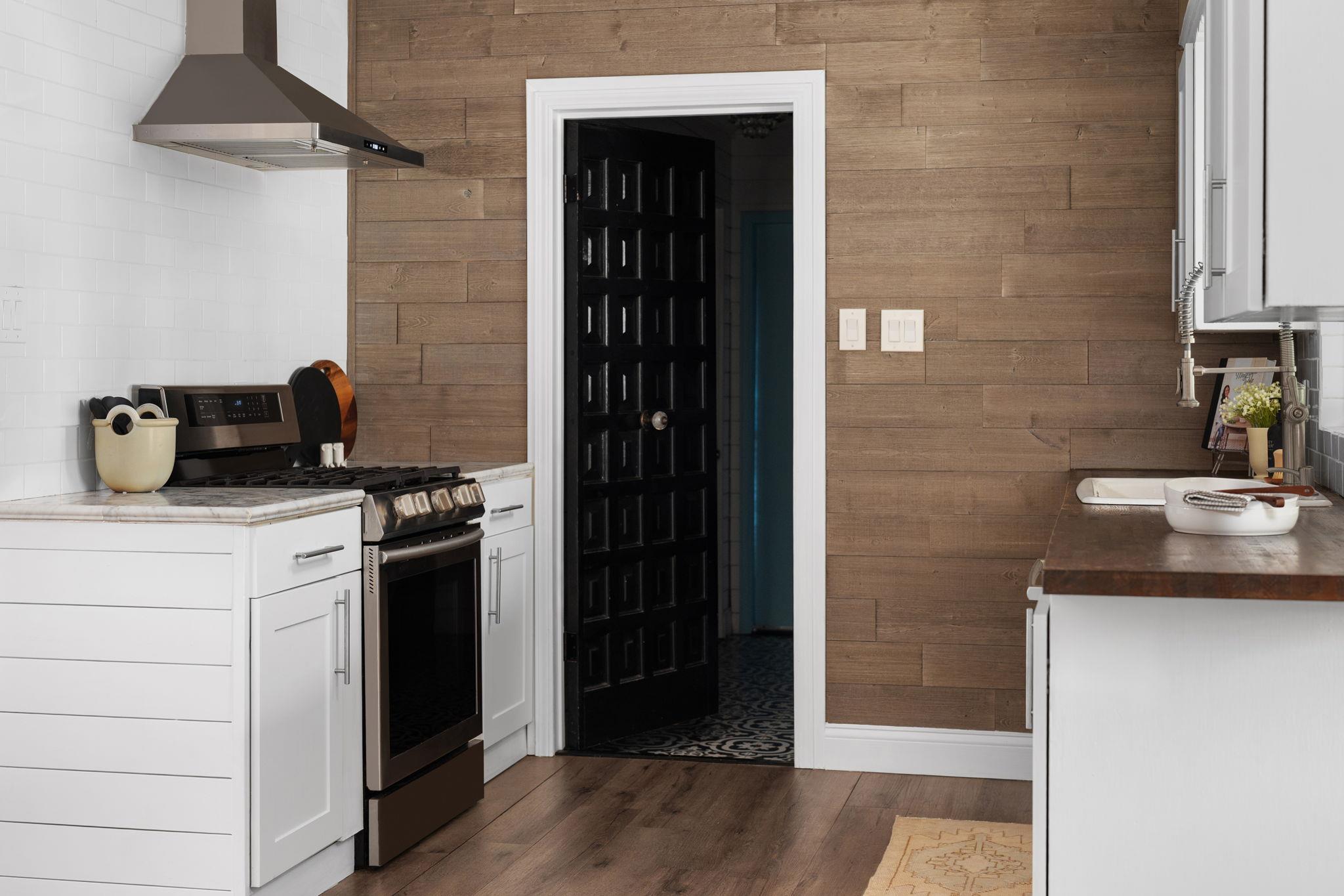Kitchen with white cabinets, stainless gas range, wood-plank wall, and black doorway.
