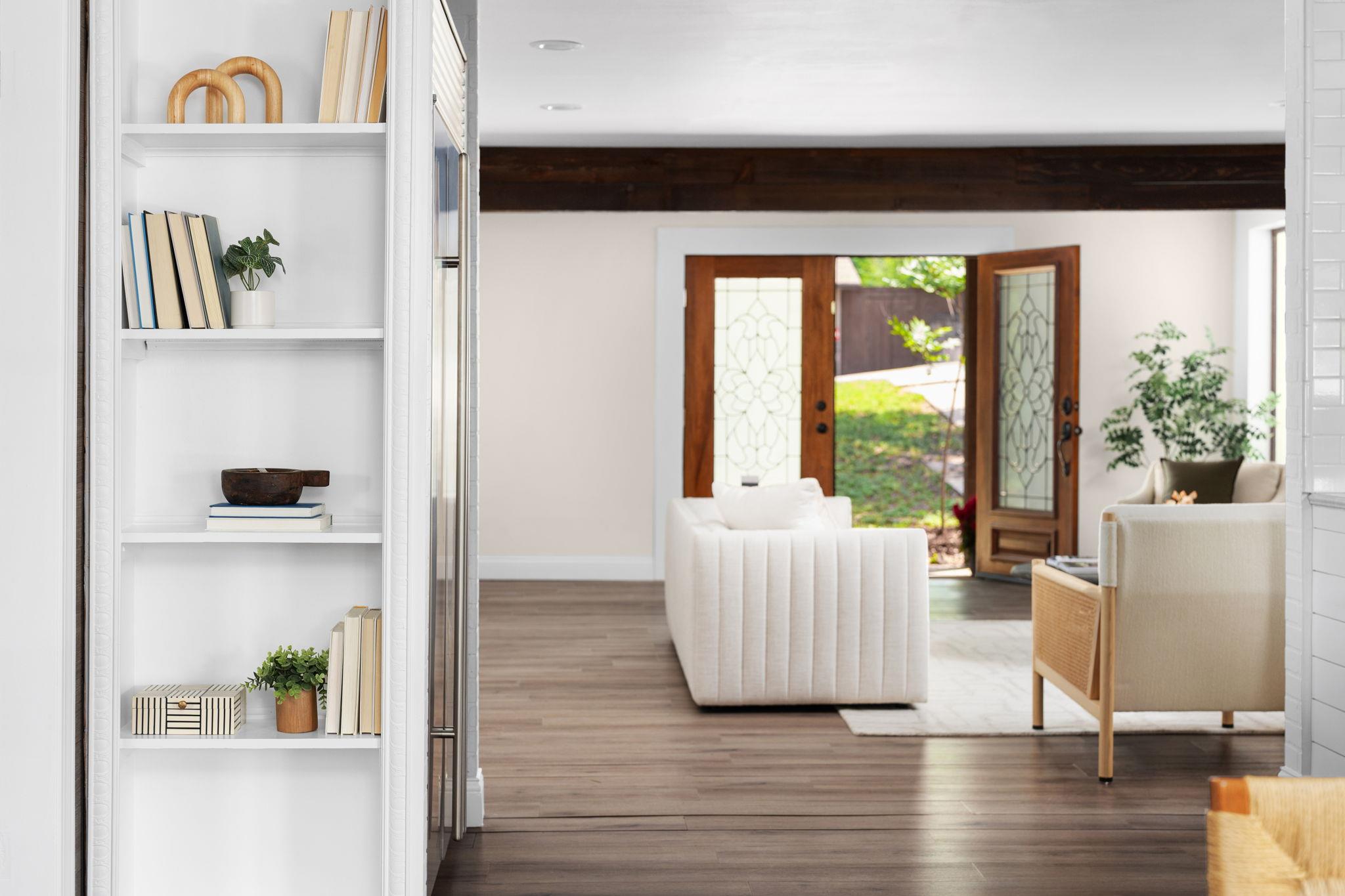 Living room with cream seating, built-in white shelves, and open glass doors to a green yard.