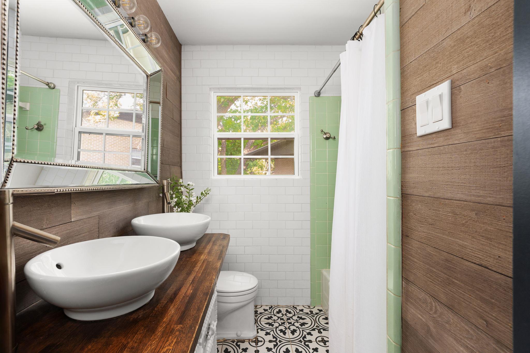 Bathroom with double vessel sinks, a dark wood vanity, pale green tile, and patterned floor.