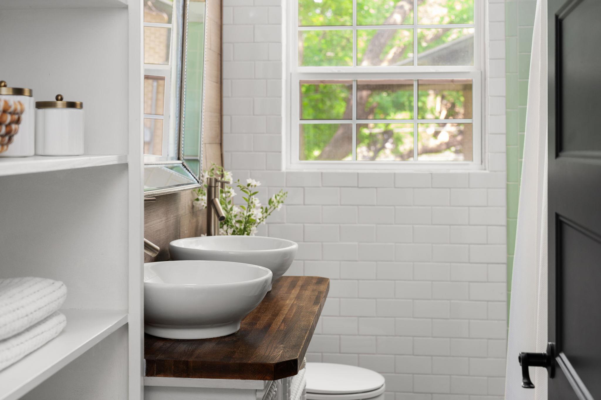 Bathroom with twin vessel sinks on a dark wood vanity beneath a large window.