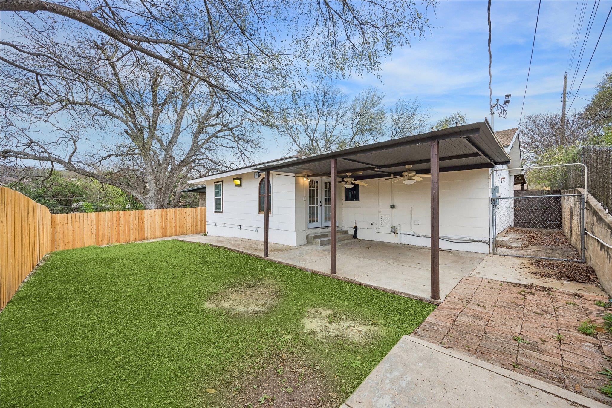 White house with a covered patio and ceiling fans beside a fenced grassy backyard.