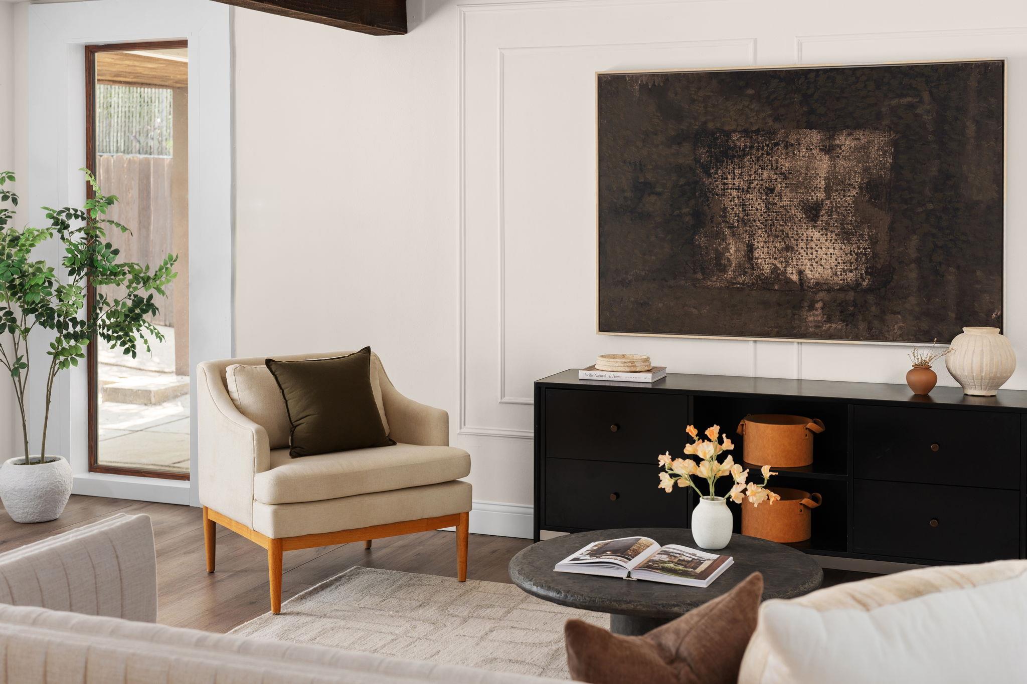 Living room with a cream armchair, dark artwork, black sideboard, and glass door to a patio.
