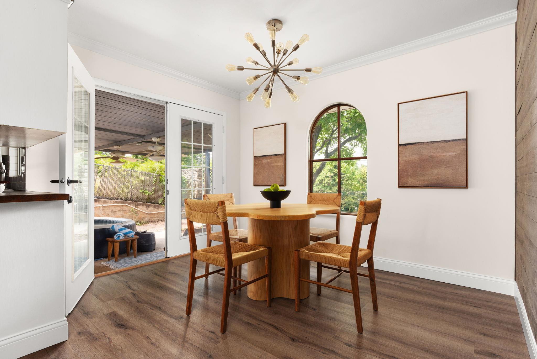 Dining room with a round wooden table, arched window, and open doors to a covered patio.