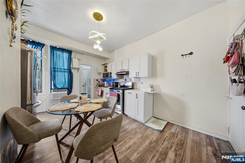 Kitchen and dining area with white cabinets, a glass table, blue curtains, and wood-look flooring.