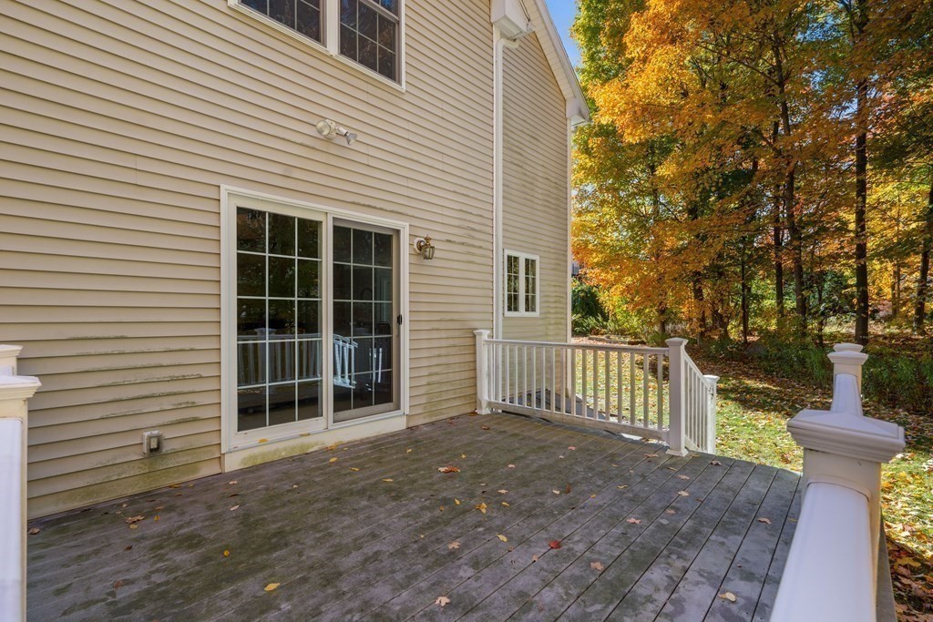 Wooden deck beside a beige-sided house, with white railings and autumn trees.