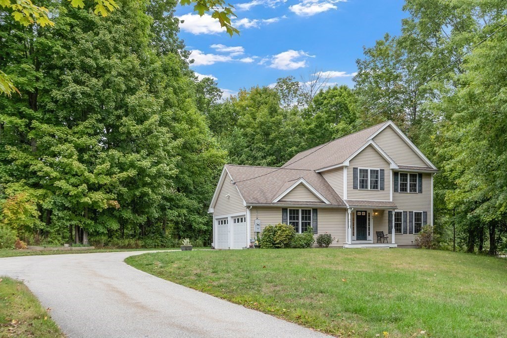 Beige two-story home with an attached double garage and curved driveway, surrounded by mature trees.