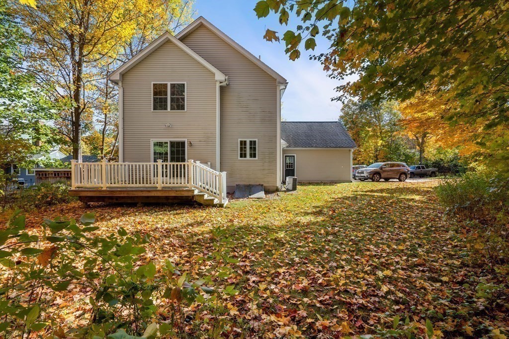 Rear of a two-story beige house with a raised deck and leaf-covered yard.