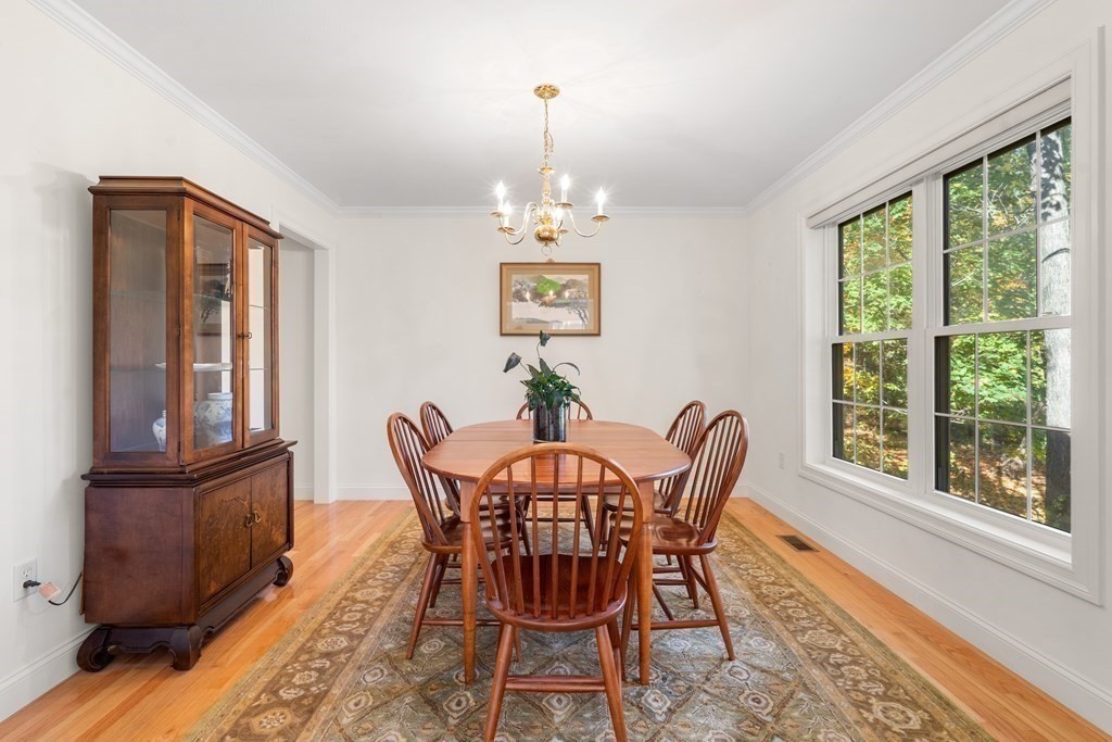 Dining room with a round wooden table, dark china cabinet, and large windows overlooking greenery.