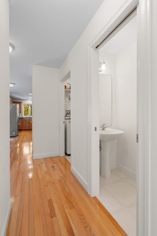 Hallway with hardwood floors, an open powder room, and the kitchen at the far end.