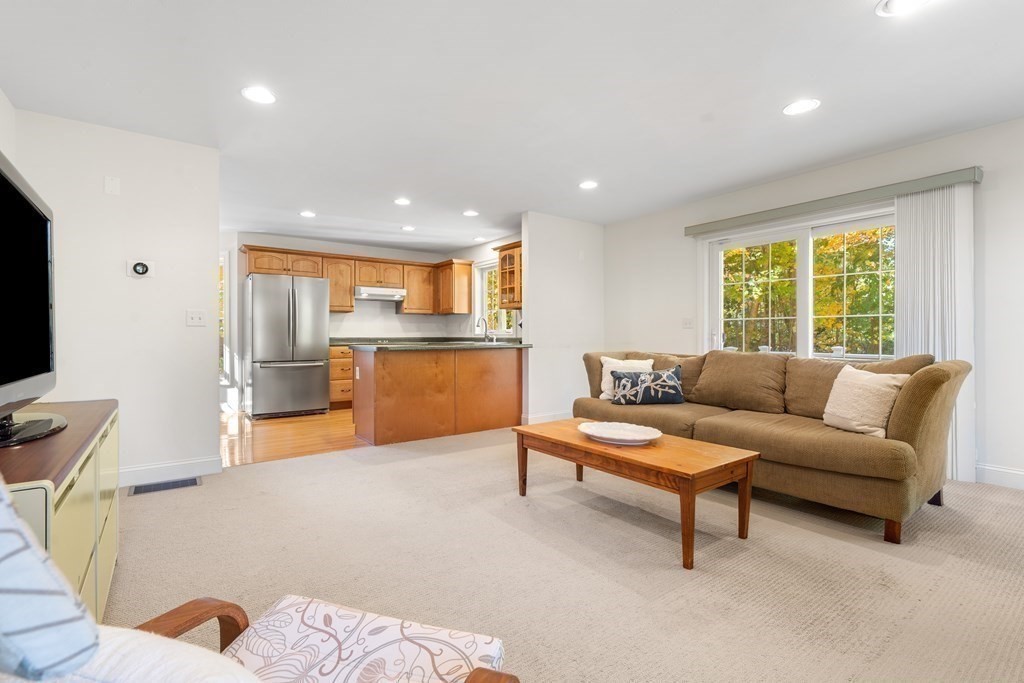 Furnished living room with a brown sofa and open kitchen, beside a window with autumn foliage.